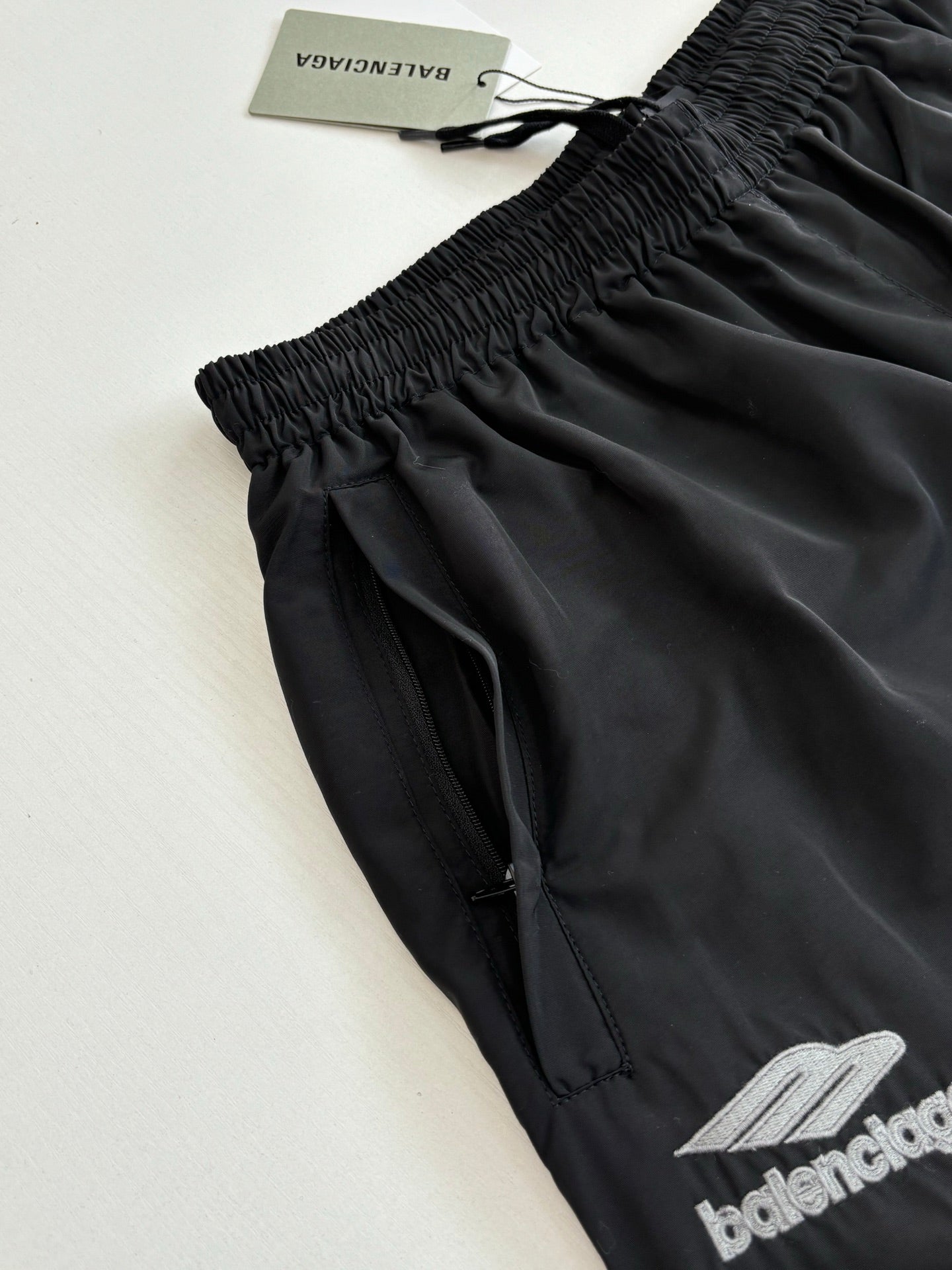 Black Balenciaga track pants close-up, elastic waistband and embroidered logo hem