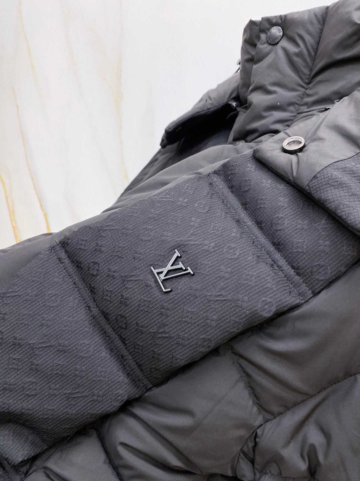 Dark gray puffer jacket sleeve with embroidered LV logo patch