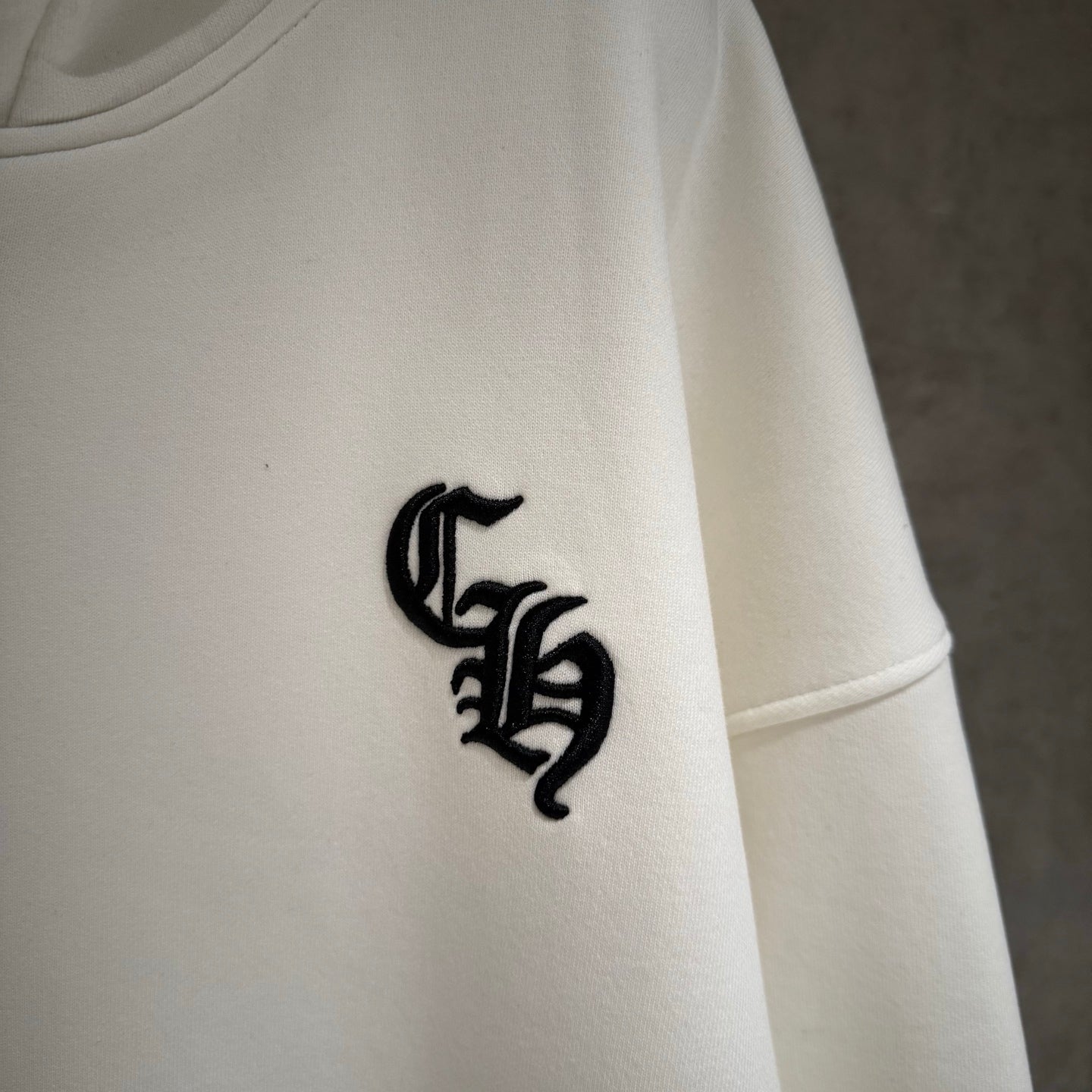 White hoodie sleeve with black embroidered emblem near the cuff