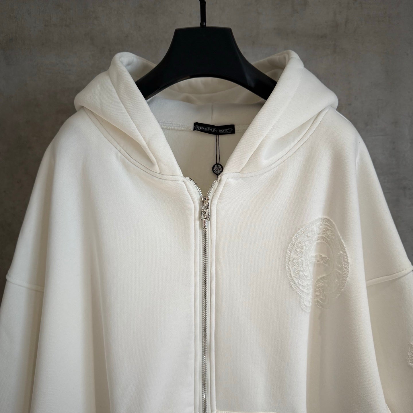 White zip-up hoodie with hood, silver-tone zipper and textured oval chest patch