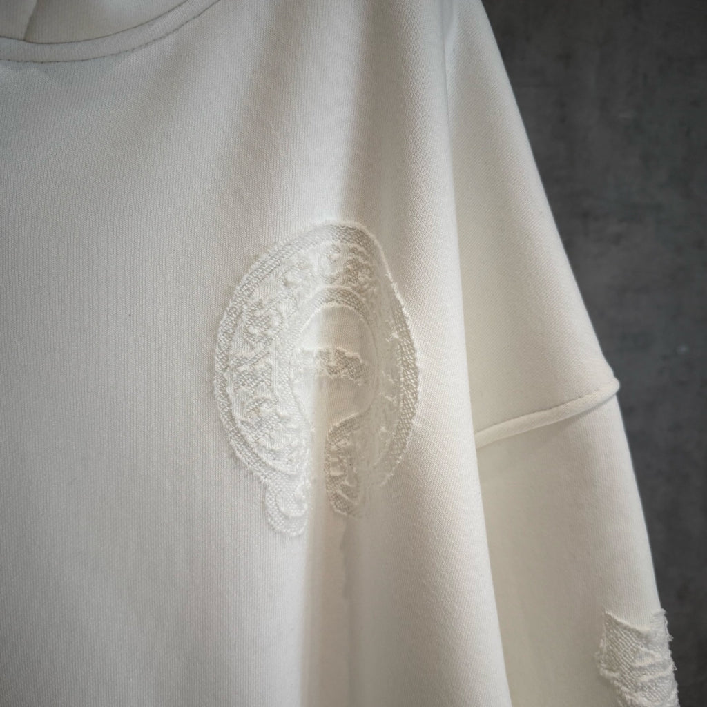 White hoodie with textured oval graphic patch on the chest