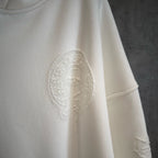 White hoodie with textured oval graphic patch on the chest