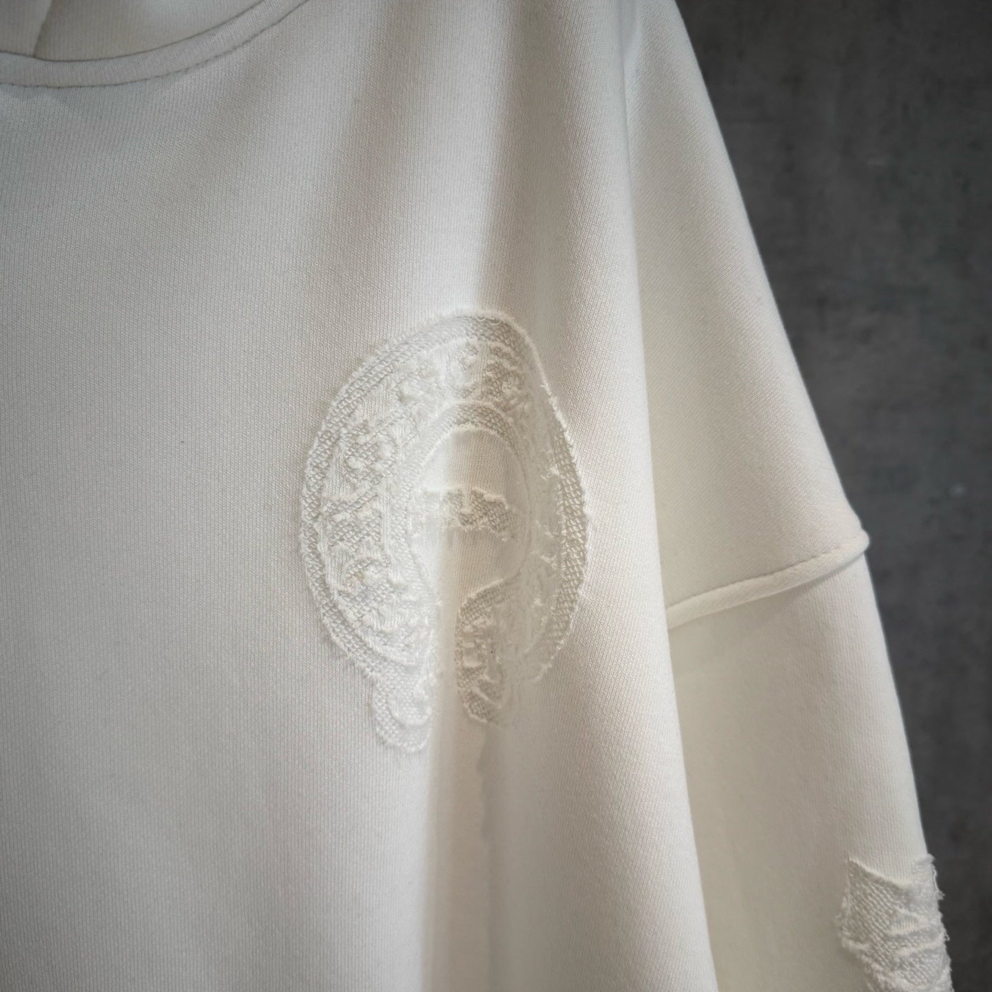 White hoodie with textured oval graphic patch on the chest