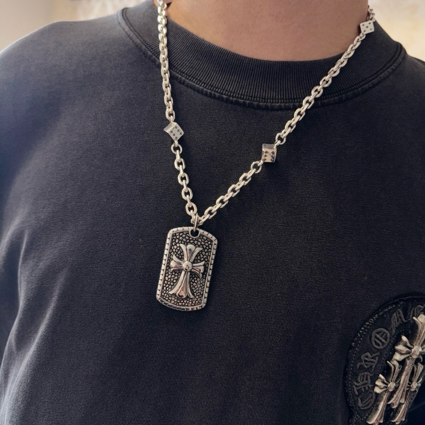 Silver-tone chain necklace with rectangular cross pendant on a dark crewneck shirt