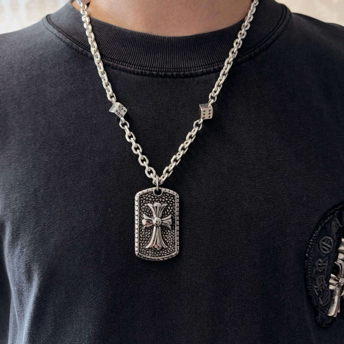 Silver-tone chain necklace with rectangular cross pendant worn on a dark crewneck shirt