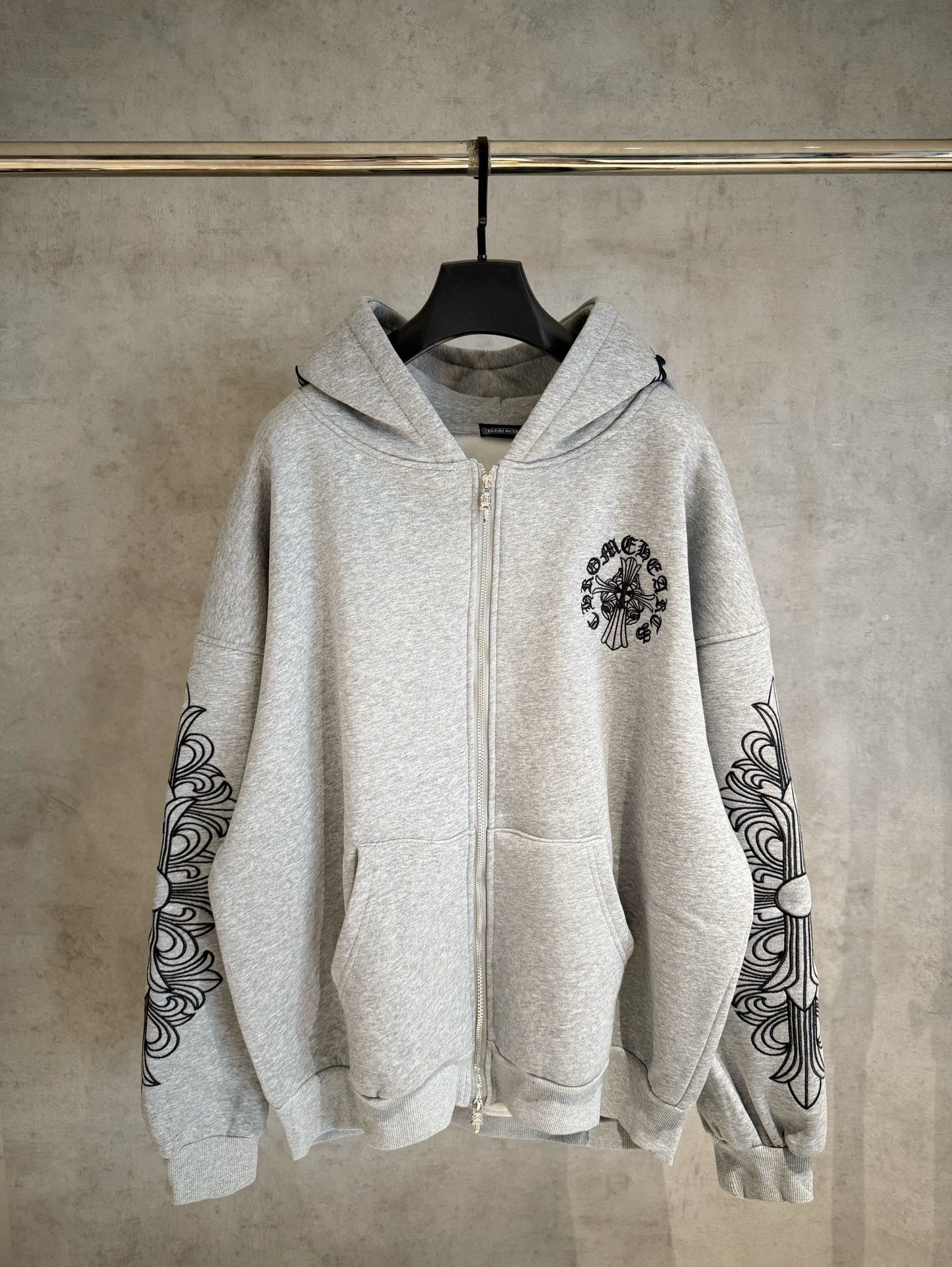 Light gray zip-up hoodie with black ornate sleeve prints and chest emblem