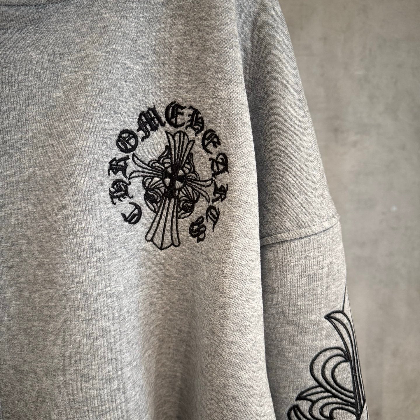 Light gray hoodie sleeve with black floral medallion print and arm swirl design