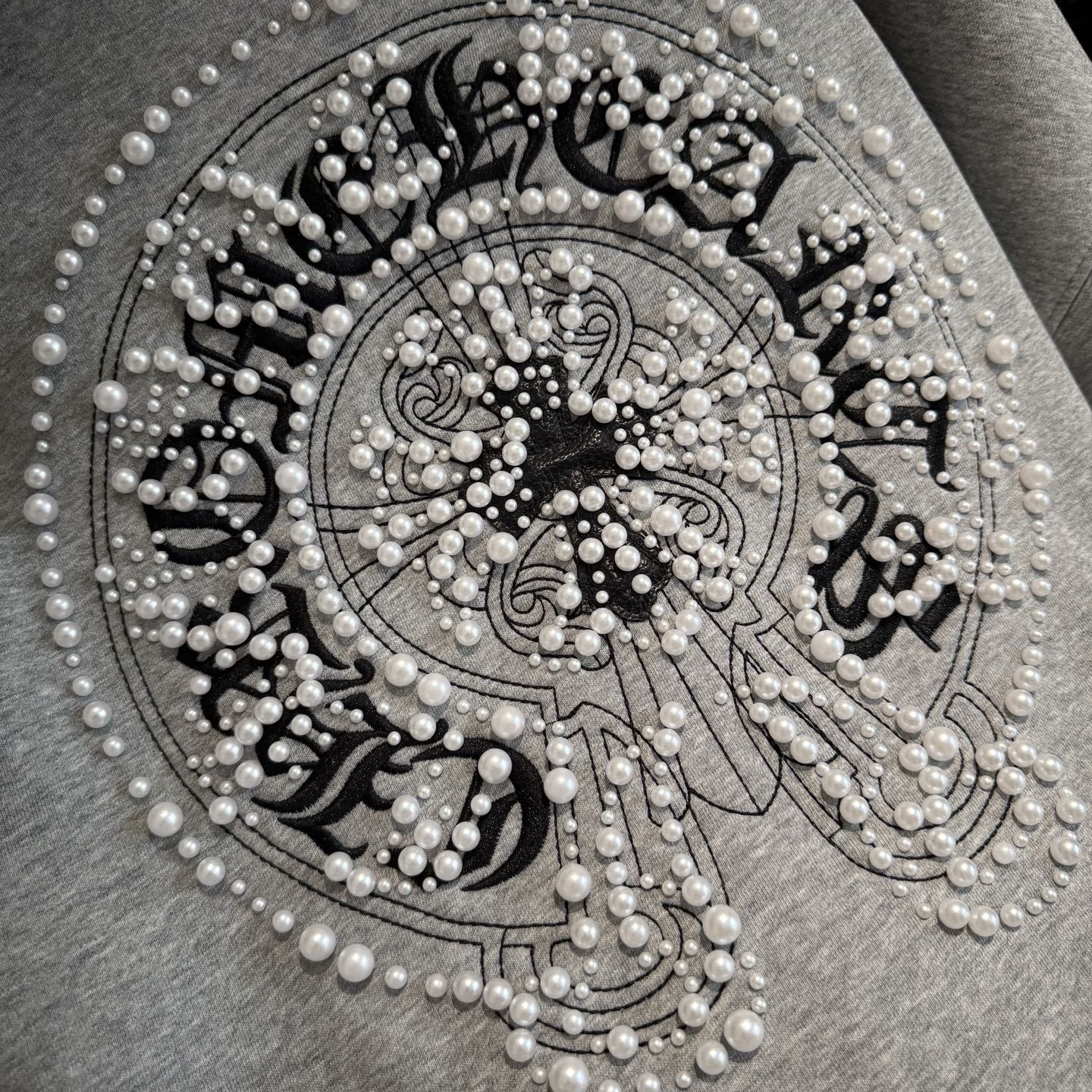Light gray hoodie front jeweled circular emblem with pearl-like bead details