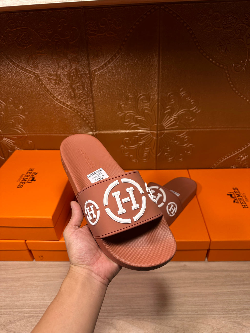 Light pink slide sandals with white logo strap, held in hand