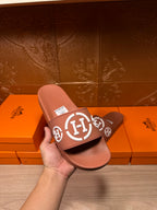 Light pink slide sandals with white logo strap, held in hand