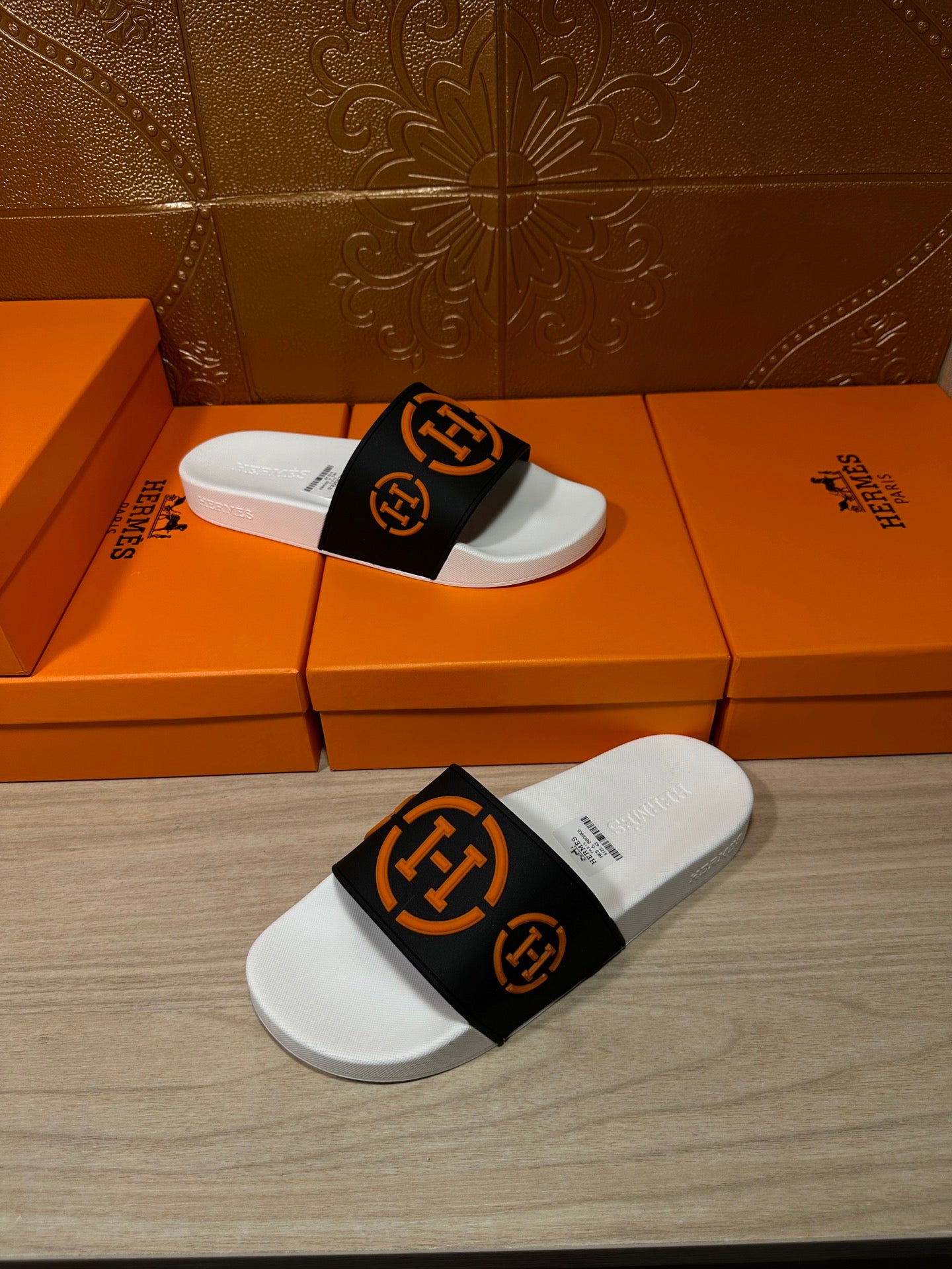 Slide sandal pair on orange shoeboxes, black strap with orange emblem and white sole