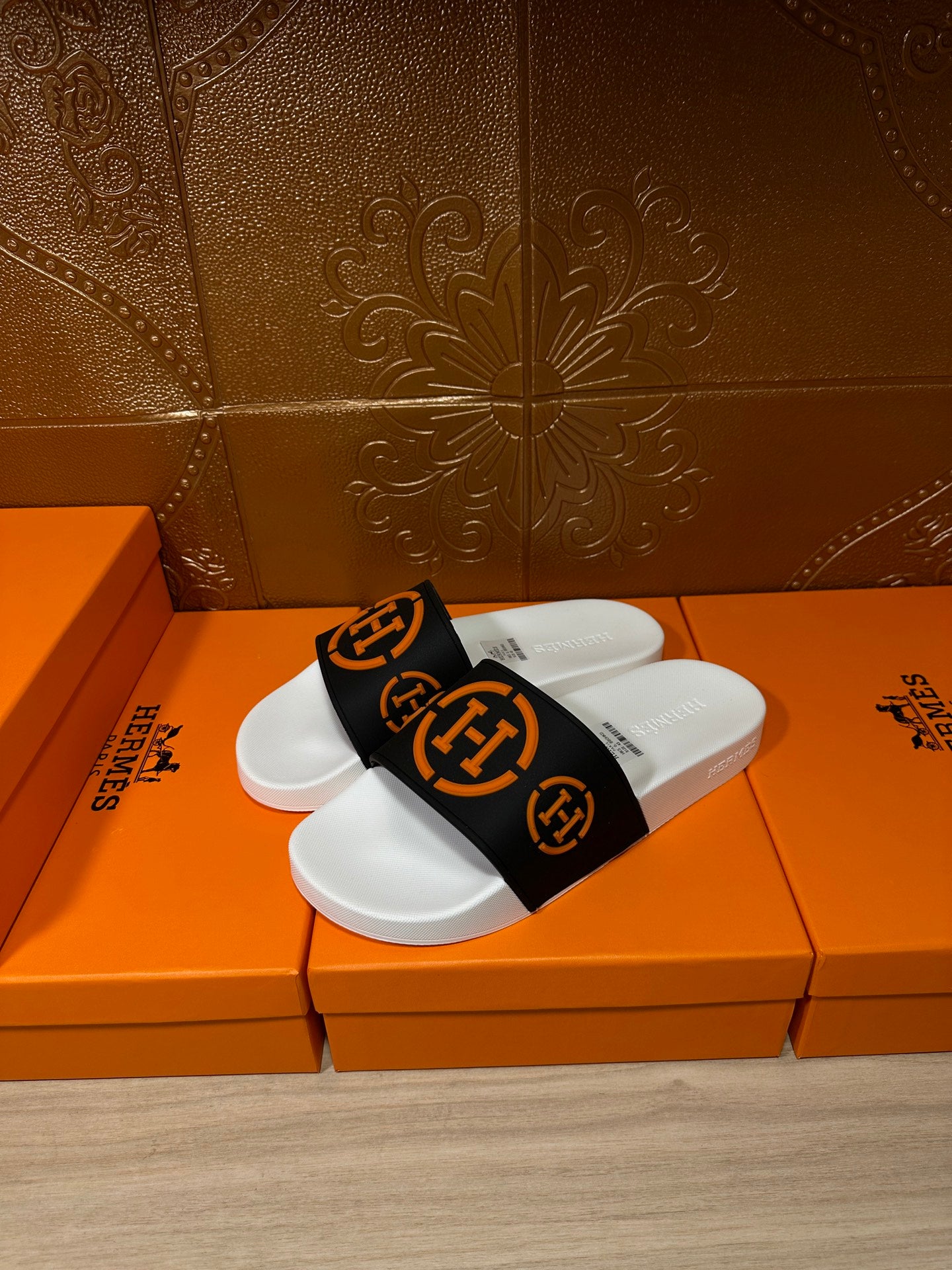 Slide sandal, black strap with orange emblem, white footbed; pair on orange shoebox