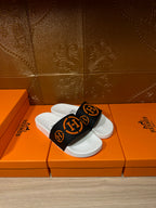 Slide sandal pair with black logo strap and white sole, set on orange storage boxes