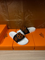 Single slide sandal with black strap and orange logo on white footbed