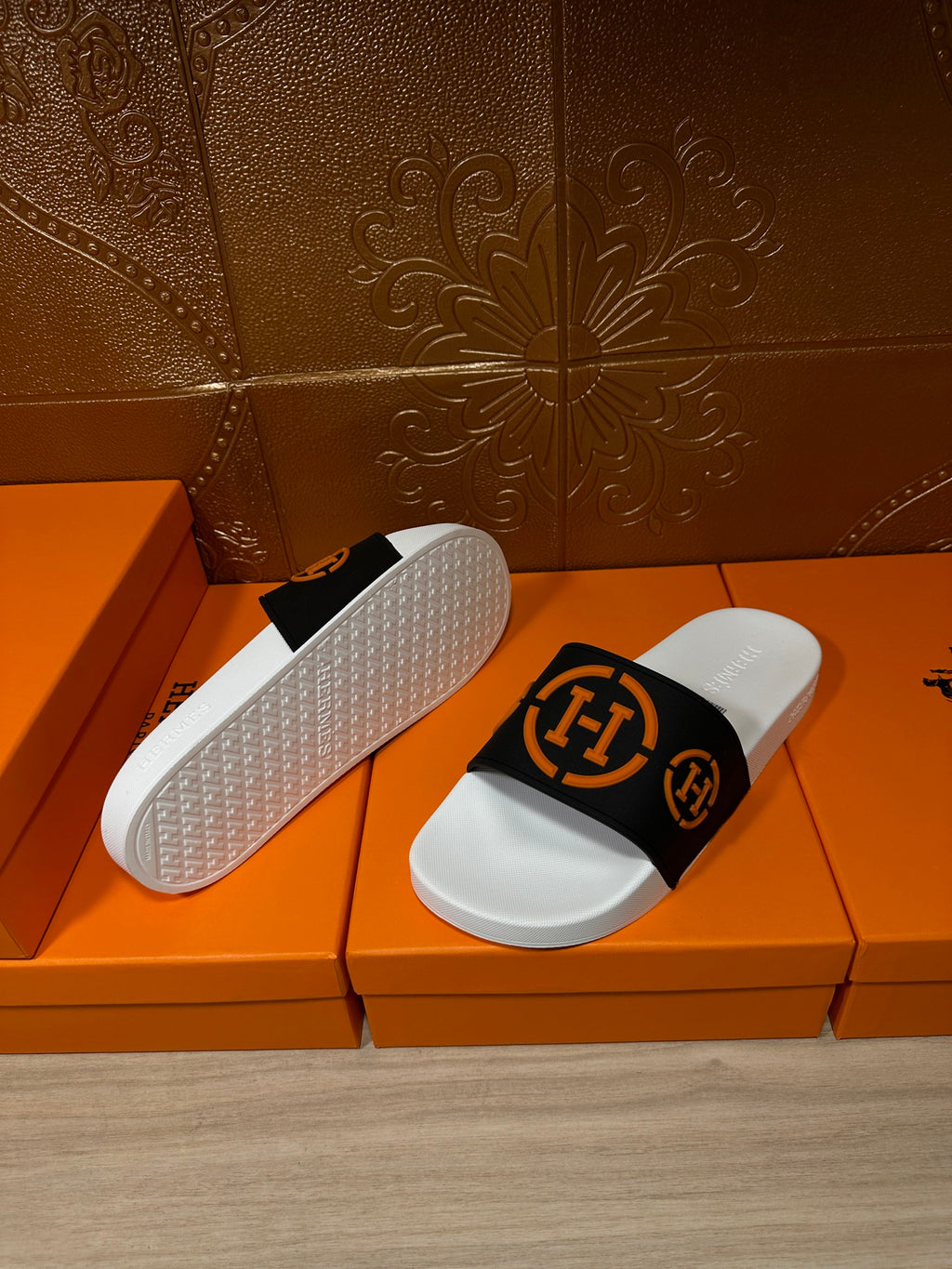Slide sandal showing textured white outsole and black strap with orange logo