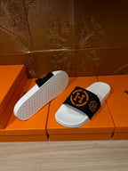 Slide sandal showing textured white outsole and black strap with orange logo