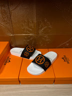 Slide sandal pair with black-and-orange logo strap and white footbed