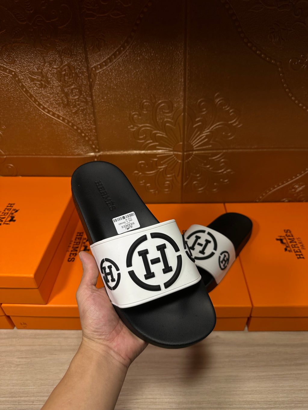 Hand holding black slide sandals with white logo strap and size label