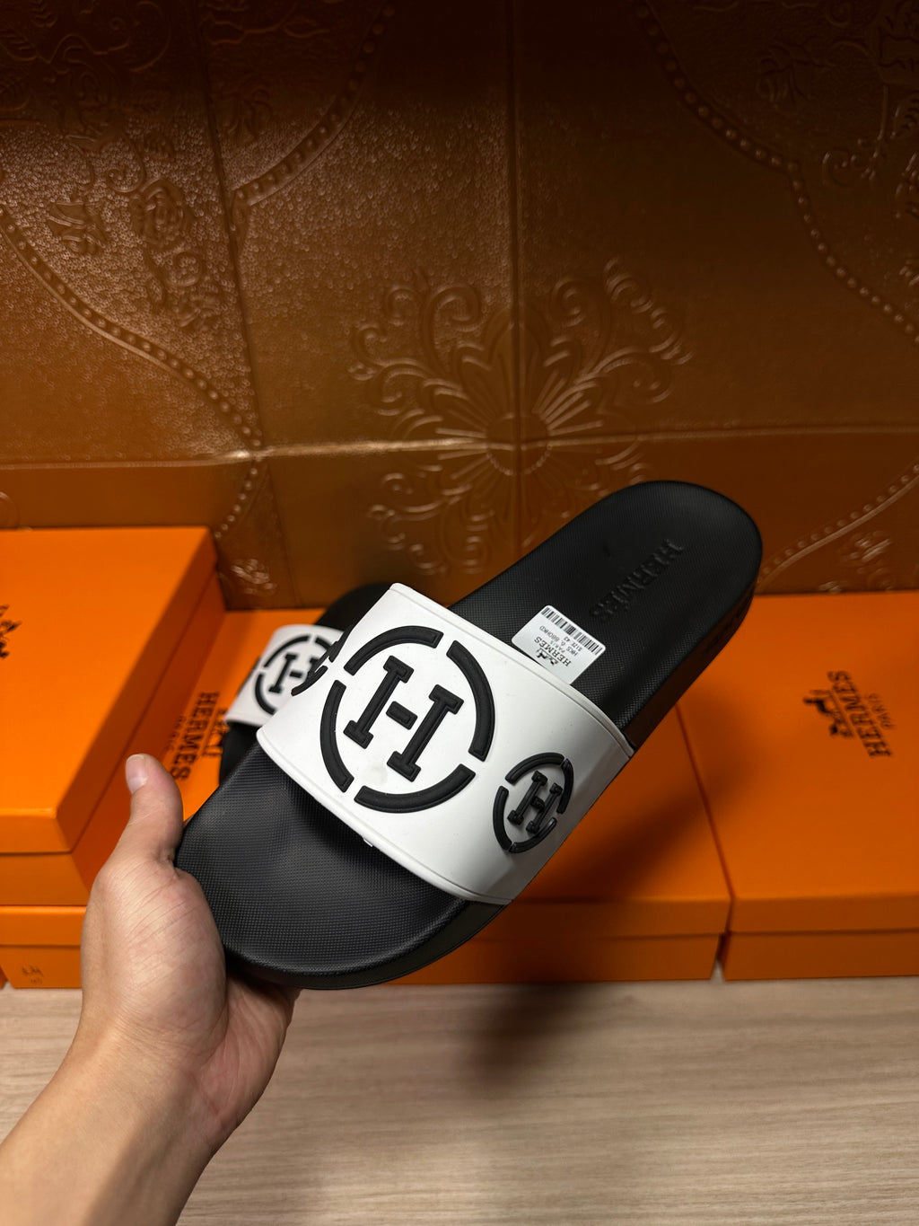 Hand holding black slide sandals with white logo strap, side view