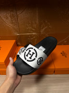 Hand holding black slide sandals with white logo strap, side view