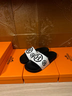 Black slide sandals with white logo band over the foot, angled view