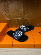 Slide sandals with navy strap and white H logo, black sole, angled on orange box
