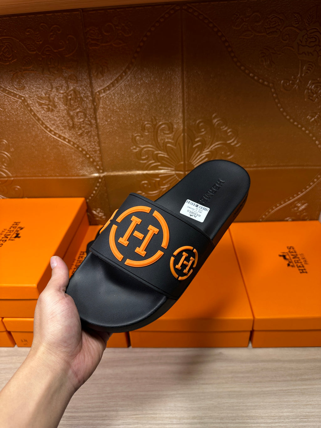 Hermes black slide sandals with orange logo strap, angled view