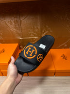 Hermes black slide sandals with orange logo strap, angled view