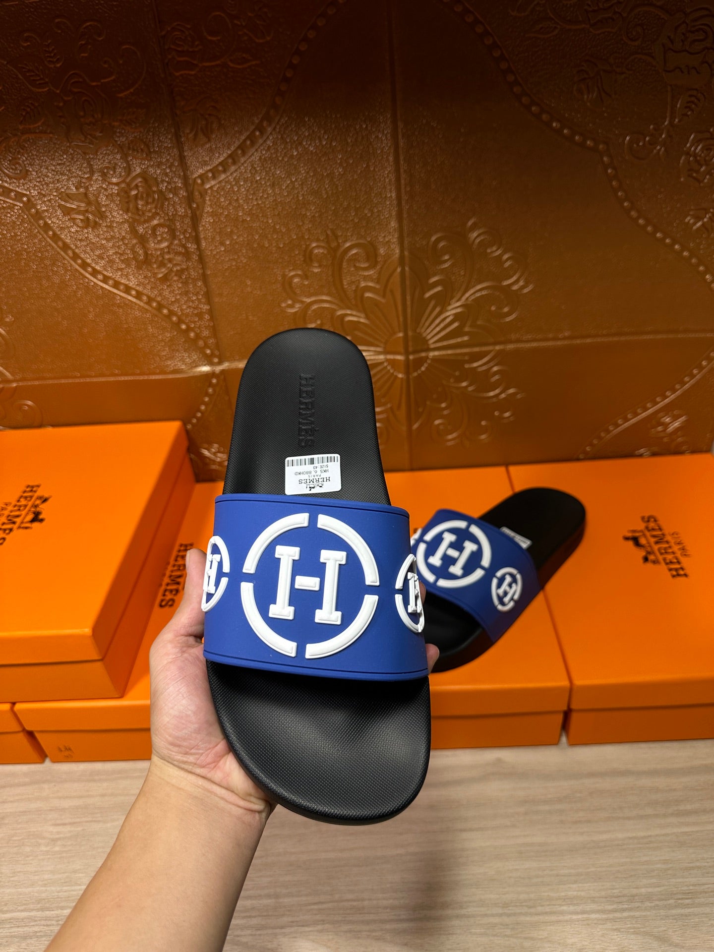 Black slide sandal held up, blue logo strap with white emblem and molded footbed
