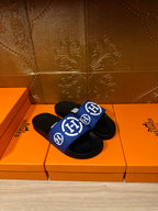 Pair of black slide sandals with blue logo straps and white emblems, side view