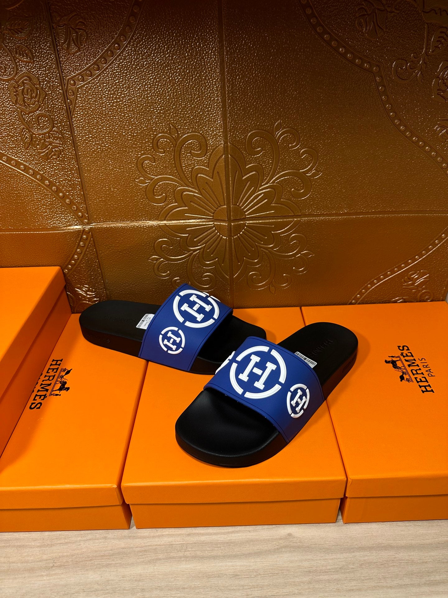 Black slide sandals with blue wide strap and white logos, two shoes shown