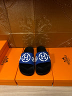 Black slide sandals with blue logo strap and white emblem, flat sole
