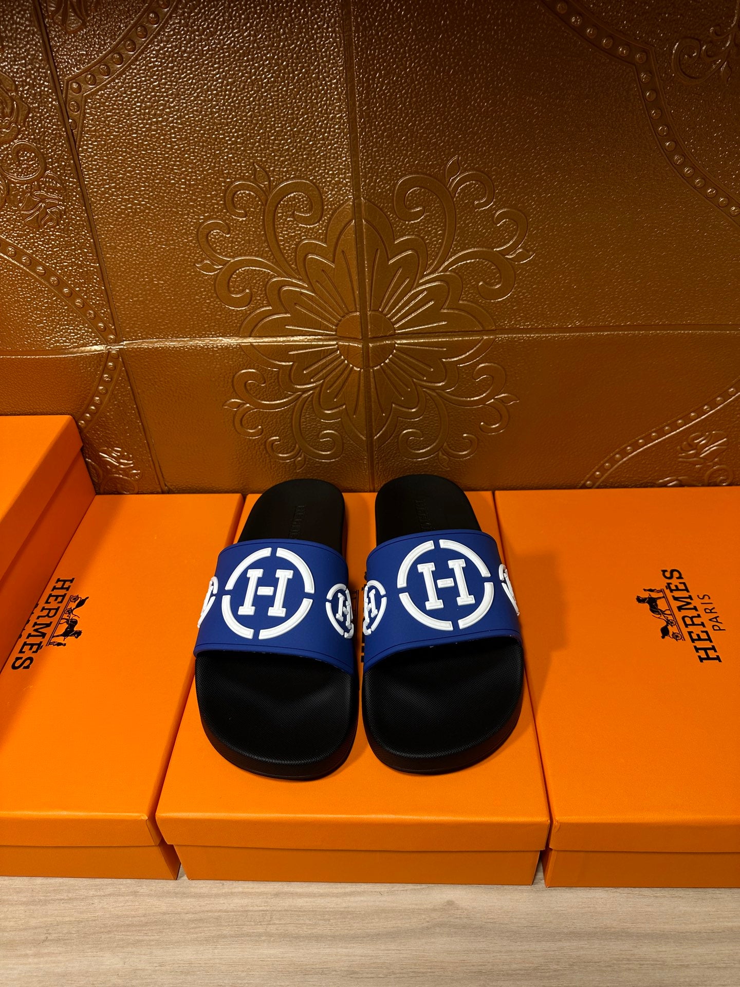 Black slide sandals with blue logo strap and white emblem, flat sole