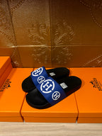 Black slide sandals with blue band strap and white H-style logo, open toe
