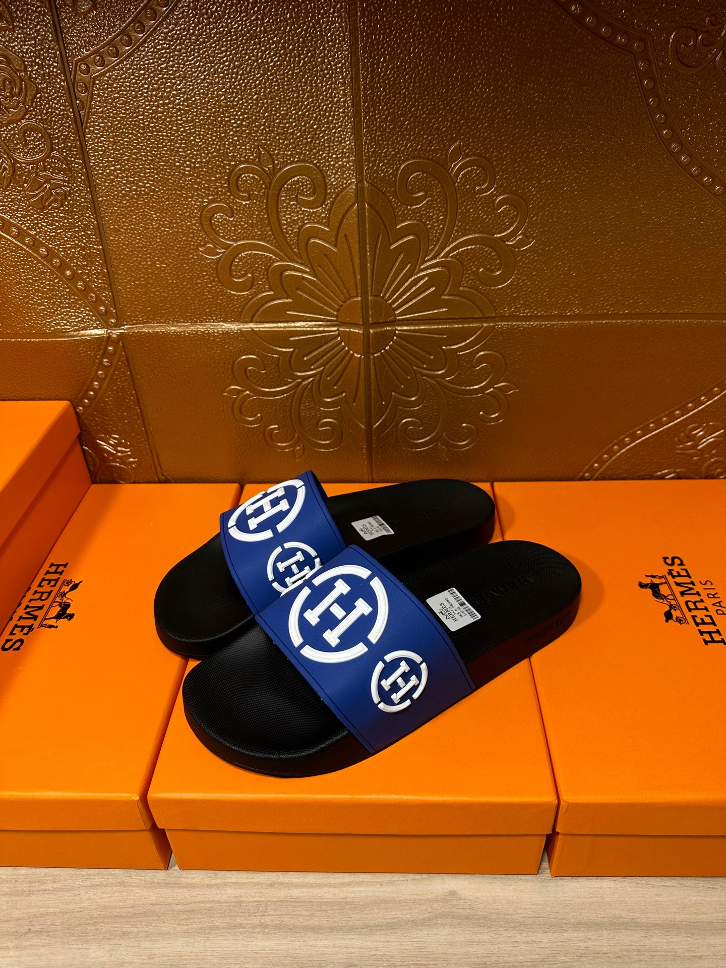 Black slide sandals with blue band strap and white H-style logo, open toe
