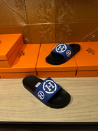 Black slide sandals with blue logo straps and white emblems, two shoes on display