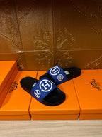 Black slide sandals with blue logo strap and white emblem, angled front view