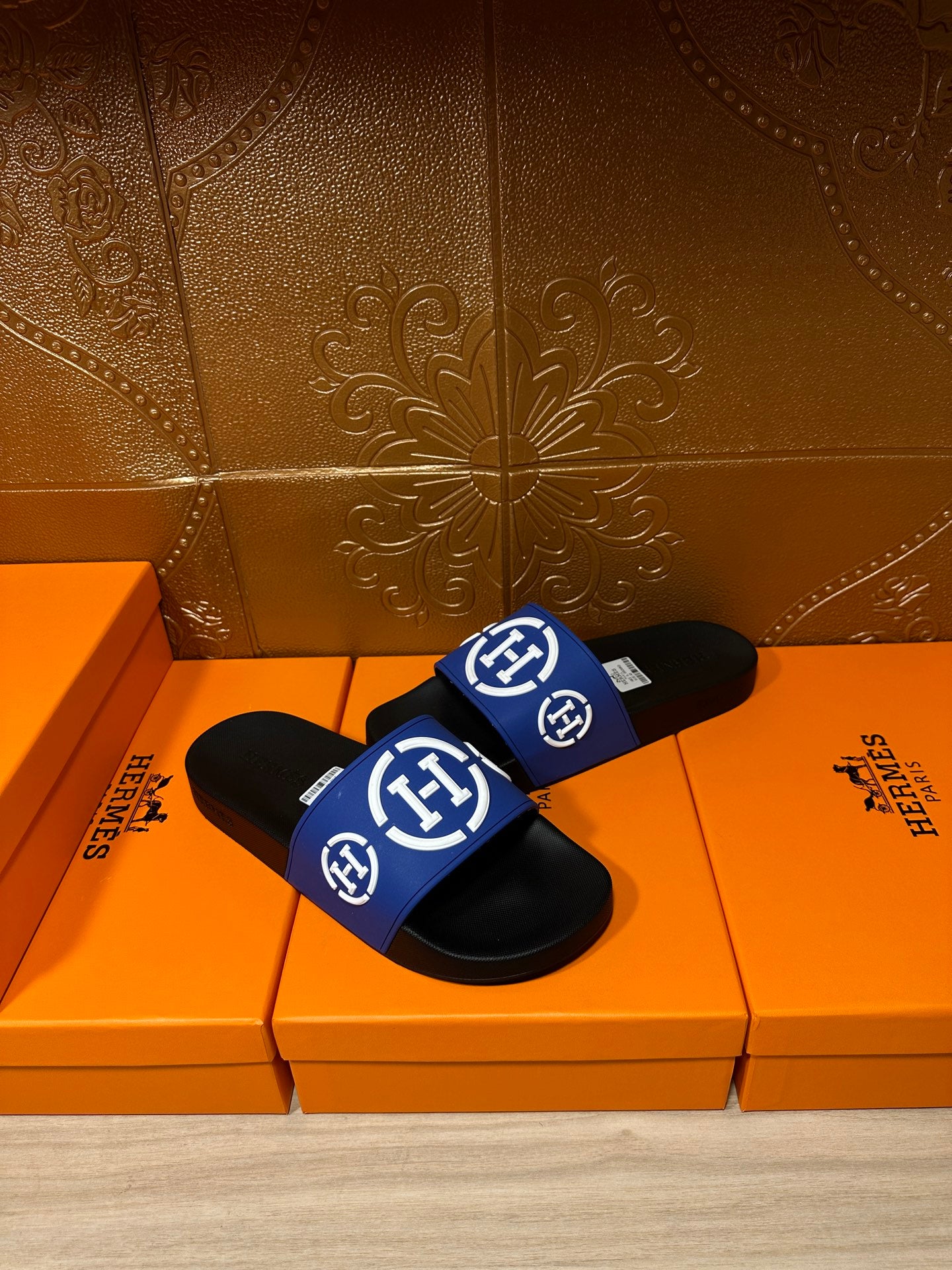 Black slide sandals with blue logo strap and white emblem, angled front view