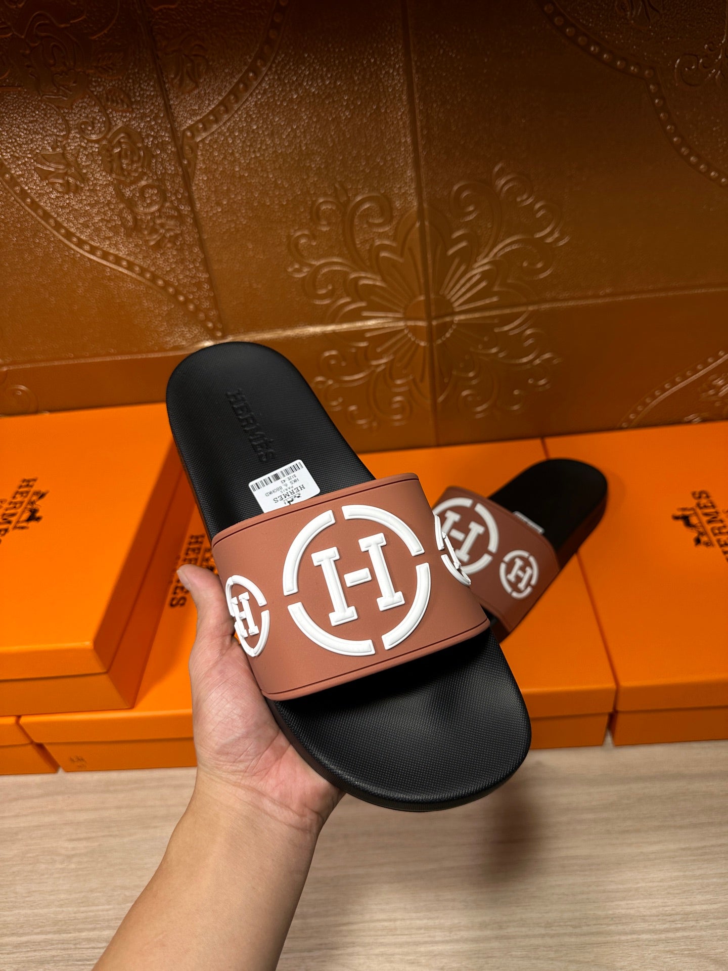 Hermes sandals held in hand: black footbed with tan strap and white H logo