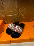 Hermes slide sandals with black soles and tan straps with white H logo detail