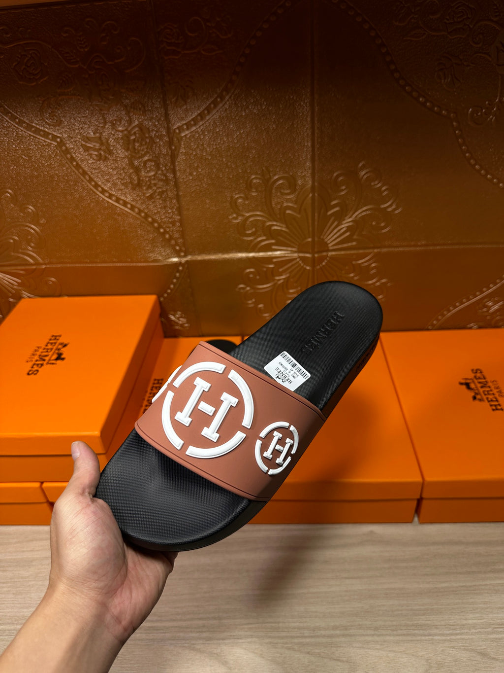 Hermes slide sandals held in hand: black footbed with tan strap and white H emblem
