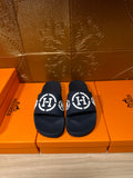 Dark slide sandals with wide strap and white emblem logo, pair on display