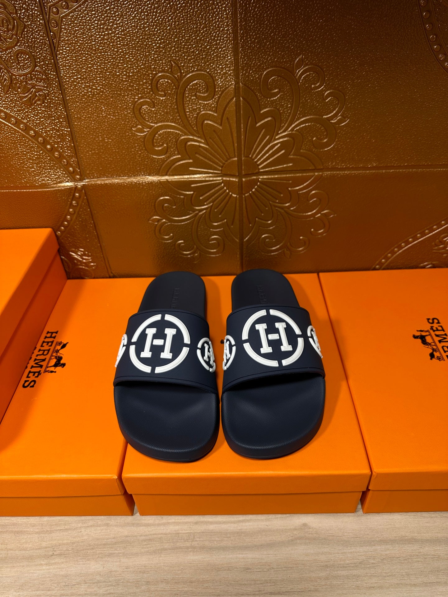 Dark slide sandals with wide strap and white emblem logo, pair on display