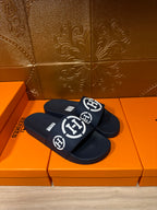 Dark slide sandals with wide front strap and white emblem logos, pair