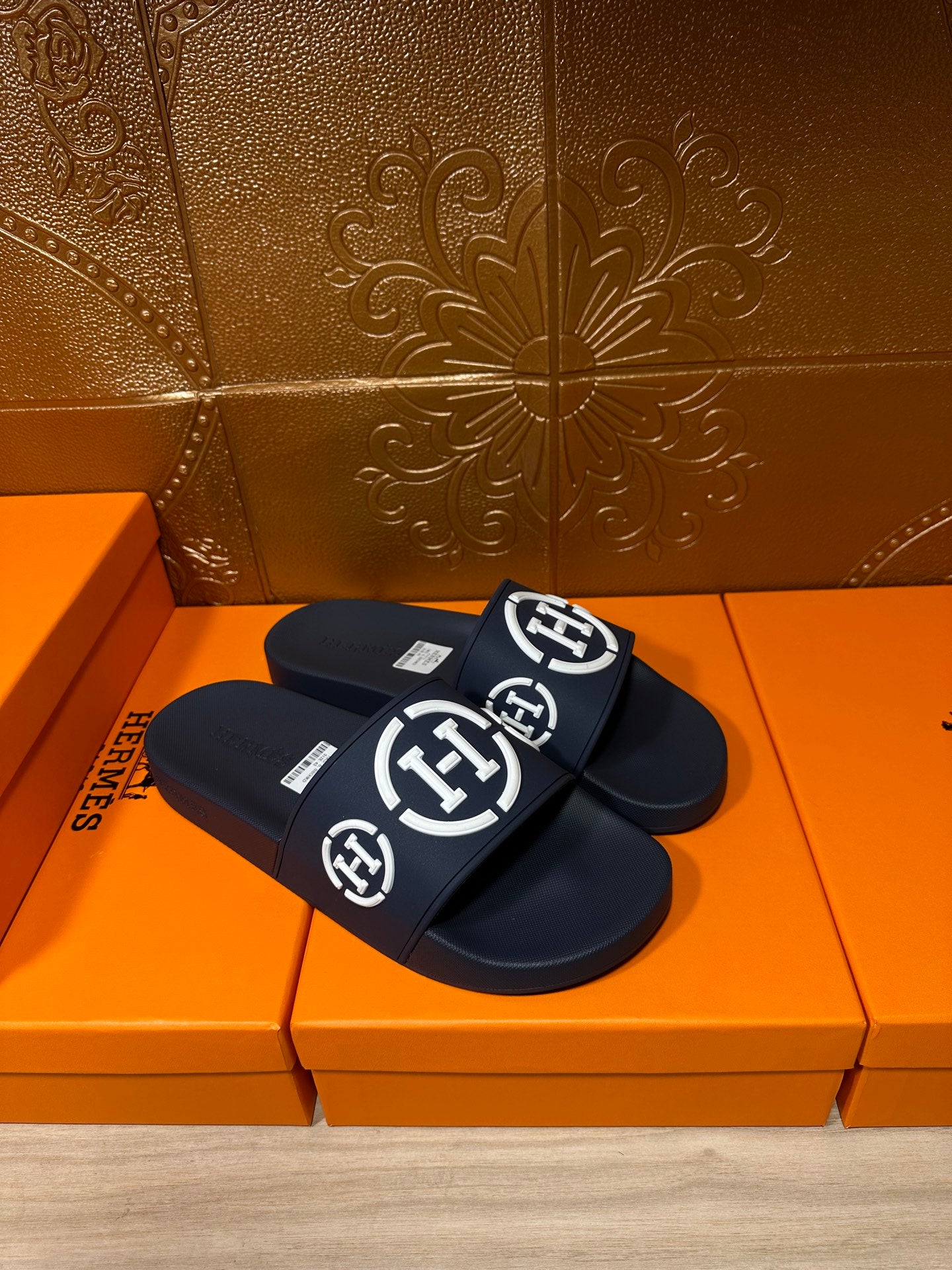 Dark slide sandals with wide front strap and white emblem logos, pair
