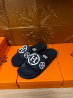Dark slide sandals with wide strap featuring white circular emblem logo, pair