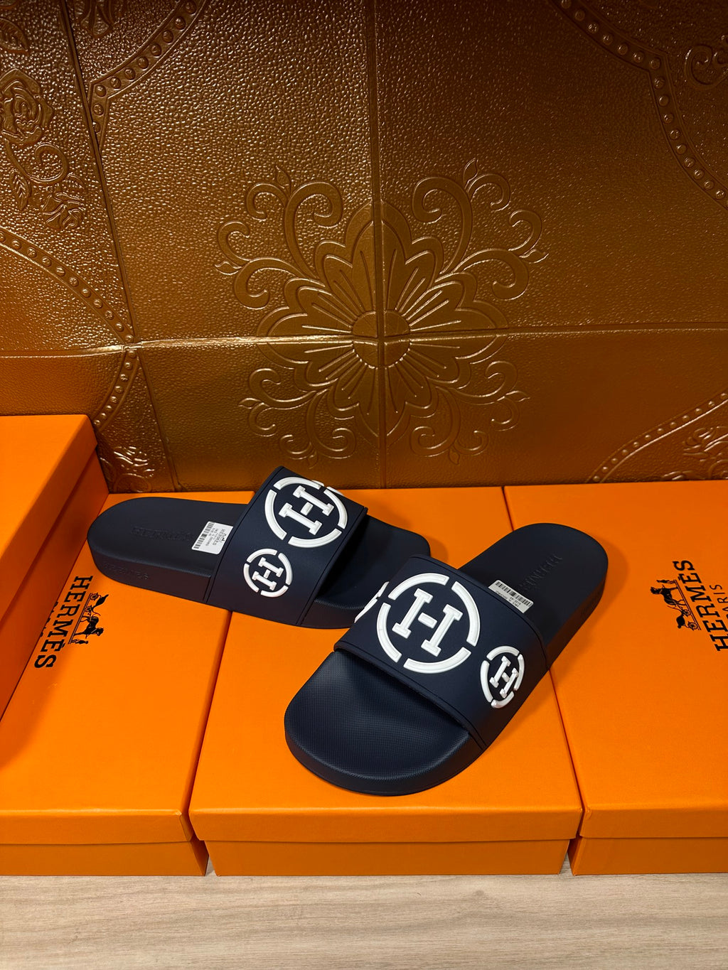 Dark slide sandals with wide strap and white emblem logos, pair laid flat