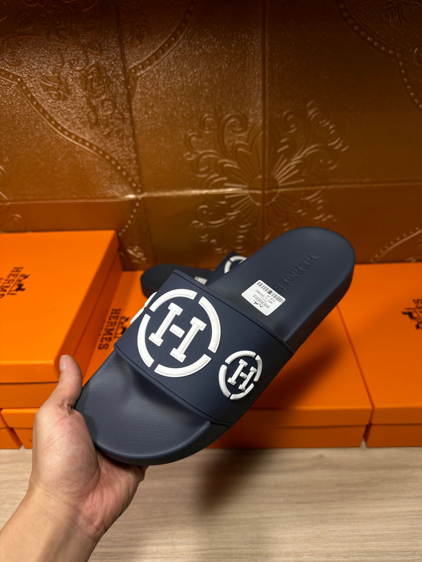 Dark slide sandal held in hand, wide strap with white emblem logo