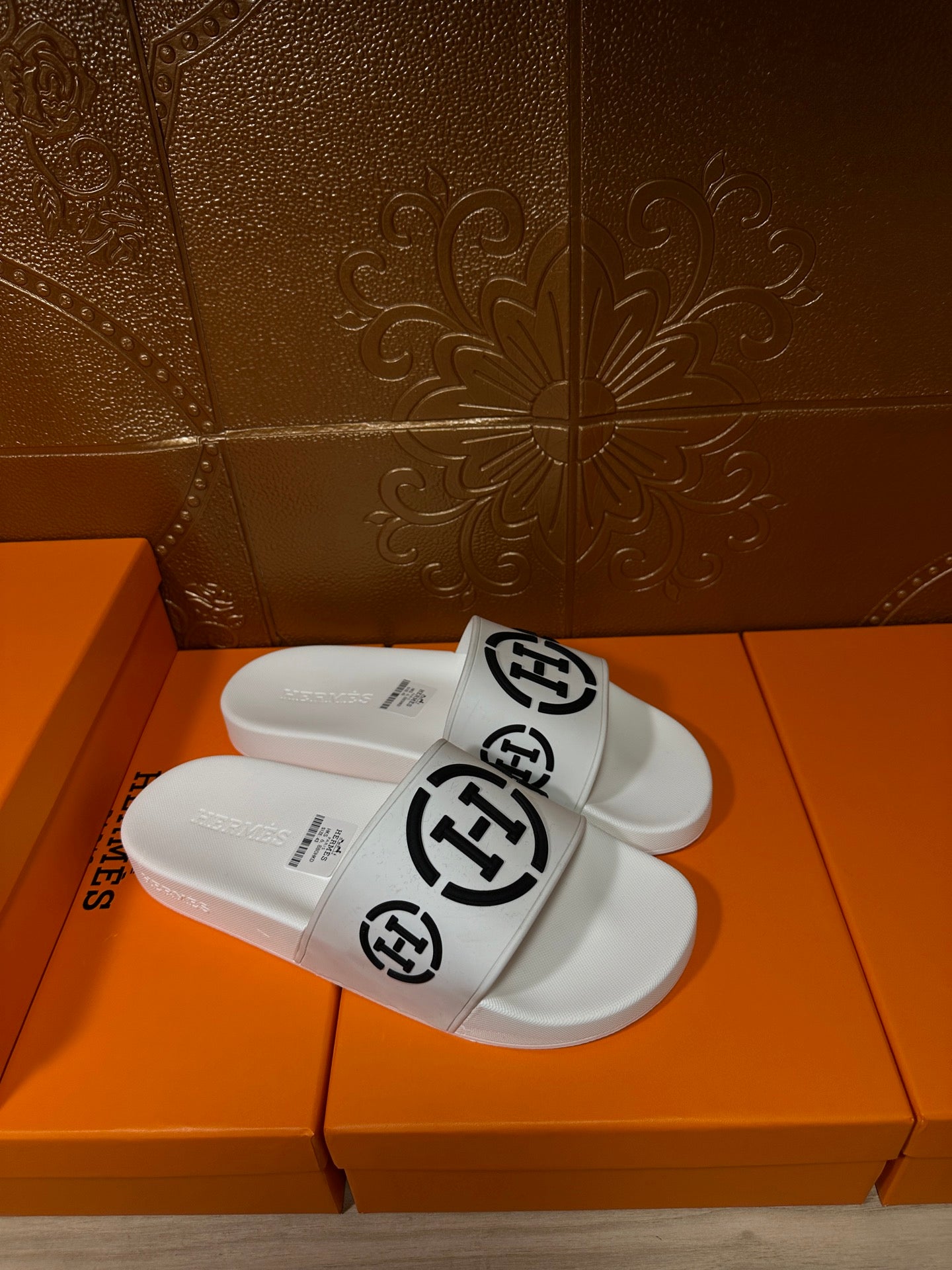 White slide sandals with black round logo on front strap