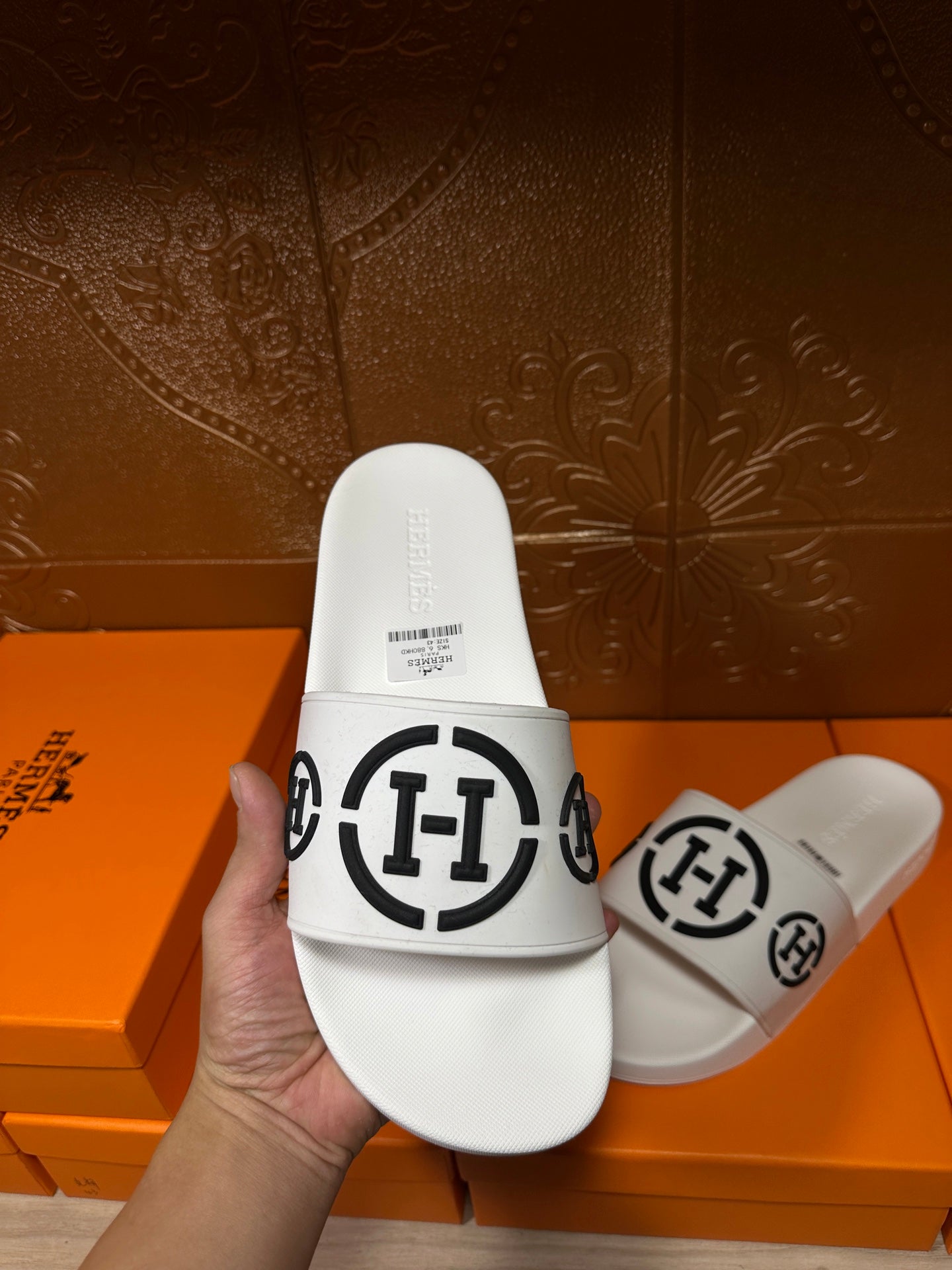 White slide sandals with black logo emblem on front strap